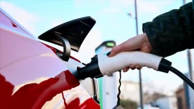 CHISINAU, MOLDOVA - Mart 2023: kırmızı Tesla Model 3 'e şarj aleti takan bir kadının yakın görüntüsü. Yavaş çekim