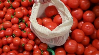 Mağazada tekrar kullanılabilir bir çantada domates toplayan bir kadın. Ekoloji ve Dünya Günü teması. Yavaş çekim