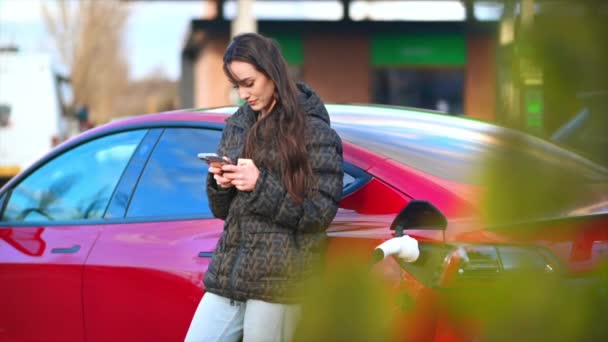 Kırmızı Elektrikli Arabasının Yanında Akıllı Telefon Kullanan Bir Kadın Görülüyor — Stok video