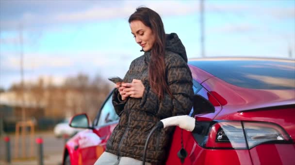 Widok Kobiety Używającej Smartfona Przy Ładowaniu Czerwonego Elektrycznego Samochodu Zwolniony — Wideo stockowe