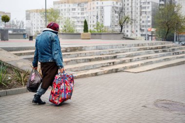 CHISINAU, MOLDOVA - Nisan 2023: Yaşlı bir kadın şehir merkezindeki kaldırımda bavulları sürüklüyor