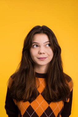 Sarı arka planda düşünen ve gülümseyen genç bir kadının portresi.