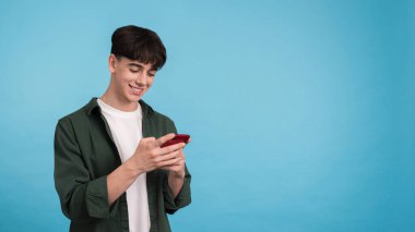 Genç adam mavi arka planda telefonunu kullanıyor.