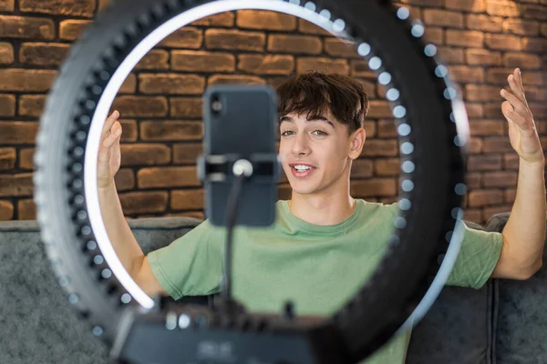 stock image A young smiling man blogger influencer talking and shooting himself on smartphone on a tripod with ring light in a studio