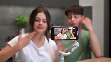 Genç gülümseyen adam ve kadın blog yazarları konuşuyorlar ve kendilerini akıllı telefondan bir mutfaktaki dengeleyiciye atıyorlar.