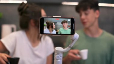 Genç gülümseyen adam ve kadın blog yazarları konuşuyorlar ve kendilerini akıllı telefondan bir mutfaktaki dengeleyiciye atıyorlar.