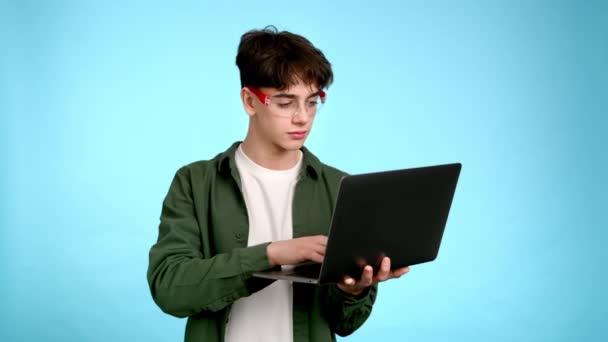 Gözlüklü Genç Adam Dizüstü Bilgisayarını Kullanıyor Mavi Arka Planda Gülümsüyor — Stok video