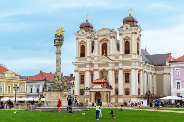 TIMISOARA, ROMANIA - Mayıs 2023: Unirii Meydanı 'ndaki St. George Katedrali manzarası. Çoklu dinlenme ve ön planda yürüyen insanlar.