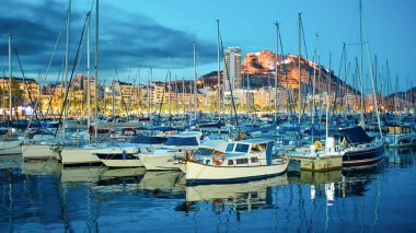 Alicante Limanı 'ndaki tekne ve yatların gece görüşü. Benacantil Dağı ve arka plandaki şehir.