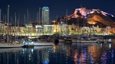 Alicante Limanı 'ndaki tekne ve yatların gece görüşü. Benacantil Dağı ve arka plandaki şehir.