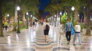 ALICANTE, İSPAN - 2023: Sokakta yürüyen insanları gece görüşü Palmiye ağaçları ve detaylı kaldırımlarla Espana 'da