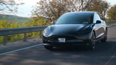 CHISINAU, MOLDOVA - MAYIS, 2023: Otoyoldaki hareketli siyah Tesla Model 3 'ün ön görüntüsü. Arka planda doğa var. Yavaş çekim