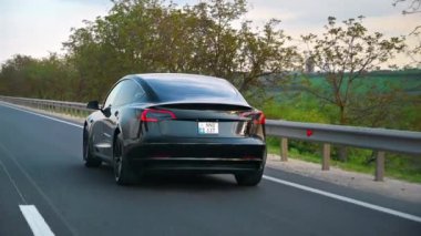 CHISINAU, MOLDOVA - MAYIS, 2023: Otoyoldaki hareketli siyah Tesla Model 3 'ün arkası. Arka planda doğa var. Yavaş çekim