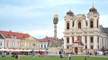 TIMISOARA, ROMANIA - 22 Mayıs 2023: Unirii Meydanı 'ndaki St. George Katedrali manzarası. Çoklu dinlenme ve ön planda yürüyen insanlar.