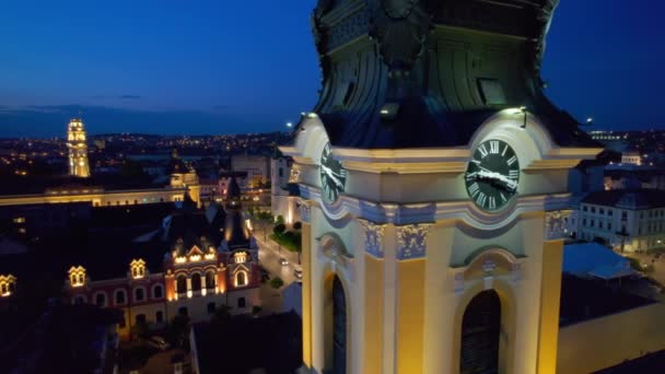 ルーマニアの夜にダウンタウンのオラデアにある聖ニコラス大聖堂の実際のドローンビュー 背景にユニリイ広場 — ストック動画