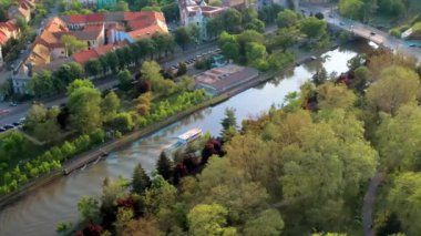 Romanya 'nın Timisoara kentindeki Bega nehrinin hava aracı görüntüsü. Nehrin her iki yakasında yüzen tekne, yeşillik ve binalar var.