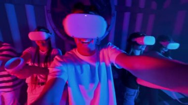 Bir grup genç arkadaş sanal gerçeklik oyunları oynuyorlar. VR ekipmanlarıyla bir arenada. Neon ışıkları