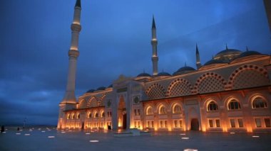 İstanbul 'daki Camlica Camii' nin akşam manzarası, Türkiye. Beyaz taştan yapılmış ön cephe, aydınlatma, önünde birkaç kişi.