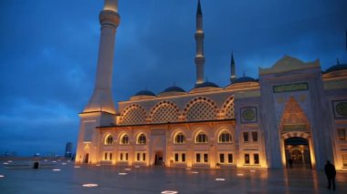 İstanbul 'daki Camlica Camii' nin akşam manzarası, Türkiye. Beyaz taştan yapılmış ön cephe, aydınlatma, önünde birkaç kişi.