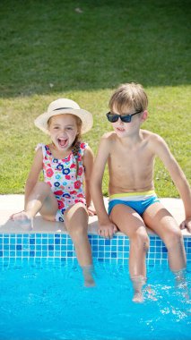 Küçük kızlar kardeşiyle havuzda su sıçratıyor.