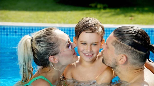 夏にプールで休んで泳ぐ父と息子と母 幸せな家族のキス — ストック写真