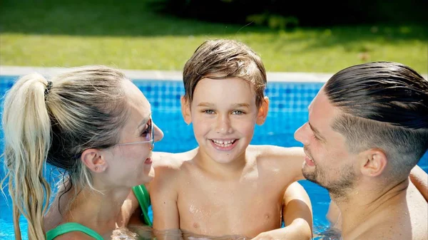 Mother with father and son resting and swimming in a pool in summer, happy family kissing