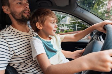 Baba küçük oğluna kucağında araba sürmeyi öğretiyor.