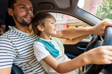 Baba küçük oğluna kucağında araba sürmeyi öğretiyor.