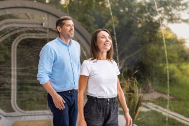 Şeffaf kabarcık çadırında gülümseyen bir çift. Çevredeki yemyeşil orman ve doğa