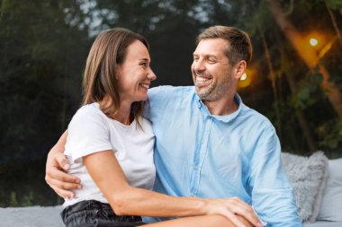 Yatakta otururken şeffaf kabarcık çadırında kucaklaşan bir çift. Arka planda yemyeşil orman