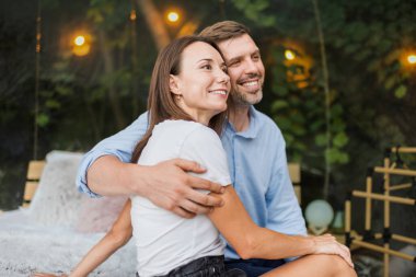 Yatakta otururken şeffaf kabarcık çadırında kucaklaşan bir çift. Arka planda yemyeşil orman