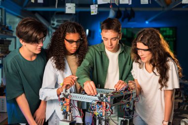 Bir laboratuvarda robotik deneyler yapan bir grup genç. Koruyucu gözlüklü kızlar