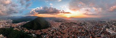 Romanya 'nın gün batımında Brasov' un panoramik hava aracı görüntüsü. Eski binalarla dolu eski şehir merkezi, yeşilliklerle kaplı tepeler