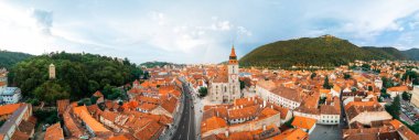 Romanya 'nın eski Brasov merkezindeki Kara Kilise' nin panoramik hava aracı görüntüsü. Etrafındaki eski binalar, hareket halindeki arabalarla dar sokaklar, yeşillikli tepeler.