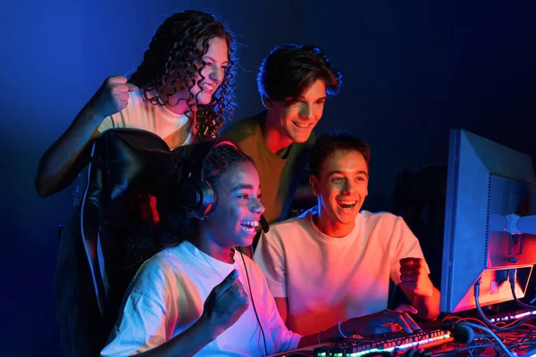 Group of multiracial teens playing video games in video game club with blue and red illumination. Excited because of a victory
