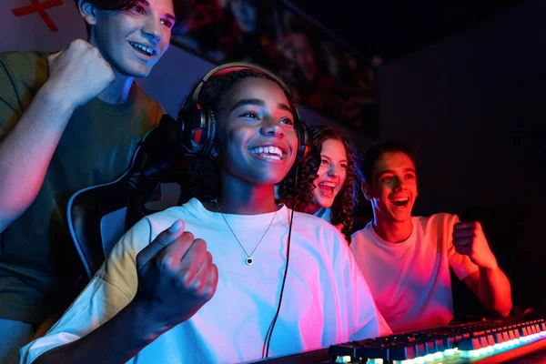Group of multiracial teens playing video games in video game club with blue and red illumination. Excited because of a victory