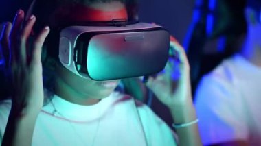 Video oyunu kulübünde aydınlatmalı video oyunu oynadıktan sonra VR kulaklığını çıkaran siyah bir genç kız.