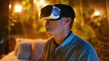 Sanal gerçeklik gözlüklü bir adam gece aydınlatmalı bir çadırda oturuyor.