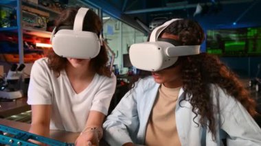 VR gözlüklü iki genç kadın bir laboratuvarda robotik deneyler yapıyor. Robot masada.