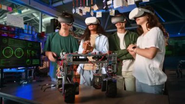 VR gözlüklü bir grup genç bir laboratuvarda robotik deneyler yapıyor ve tartışıyorlar. Robot masada.