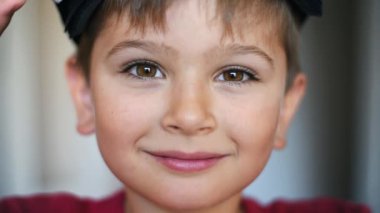 Sarışın küçük çocuk kameraya bakıyor ve VR kulaklığı takıyor.