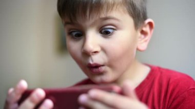 Heyecanlı sarışın çocuk akıllı telefondan video izliyor.