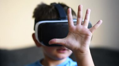 Sarışın küçük çocuk VR kulaklık kullanıyor ve el kol hareketi yapıyor.