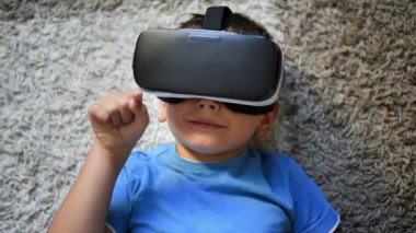 Sarışın, küçük bir çocuk halının üzerinde VR kulaklık takıyor ve el kol hareketi yapıyor.