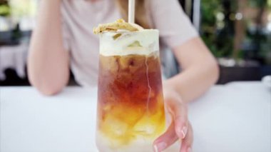 Soğuk bir espresso içen bir kadının yakın görüntüsü. Bir kafede köpük ve samanla içki.