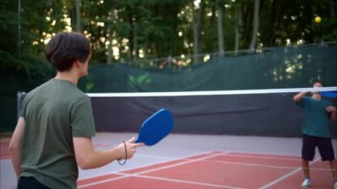 Sahada sarı top ve mavi raket oynayan çocuklar.