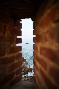 Fransa 'nın Cannes kentindeki eski bir kalenin dar penceresinden görünen yüzen bir yelkenlinin dikey görüntüsü