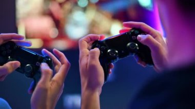 CHISINAU, MOLDOVA - 9 Eylül 2023: İki genç arkadaş oyun konsolu kullanarak oyun konsolu oynuyorlar, ellerin yakın görüntüsü, arka planda TV. Mavi ve kırmızı aydınlatma