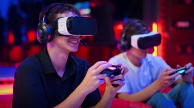 İki genç arkadaş oyun konsolu olarak VR kulaklıkları ve kulaklıklarla oyun konsolu oynuyorlar. Oyun bloknotları kullanarak, fasulye çuvallarının üzerinde otururken konuşup gülümsüyorlar. Mavi ve kırmızı ışık. Yavaş çekim