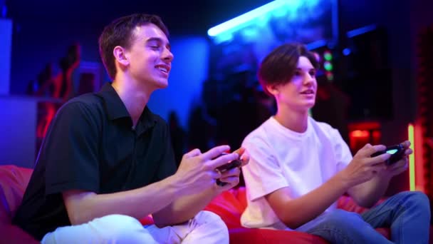 Δύο Έφηβοι Φίλοι Παίζουν Μια Κονσόλα Παιχνιδιών Χρησιμοποιώντας Gamepads Μιλώντας — Αρχείο Βίντεο